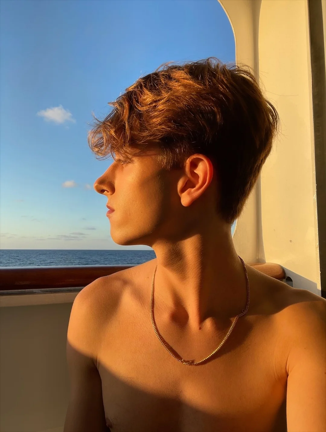 Compagnon gay Paris en voyage — profil torse nu au coucher de soleil en mer, lumière dorée