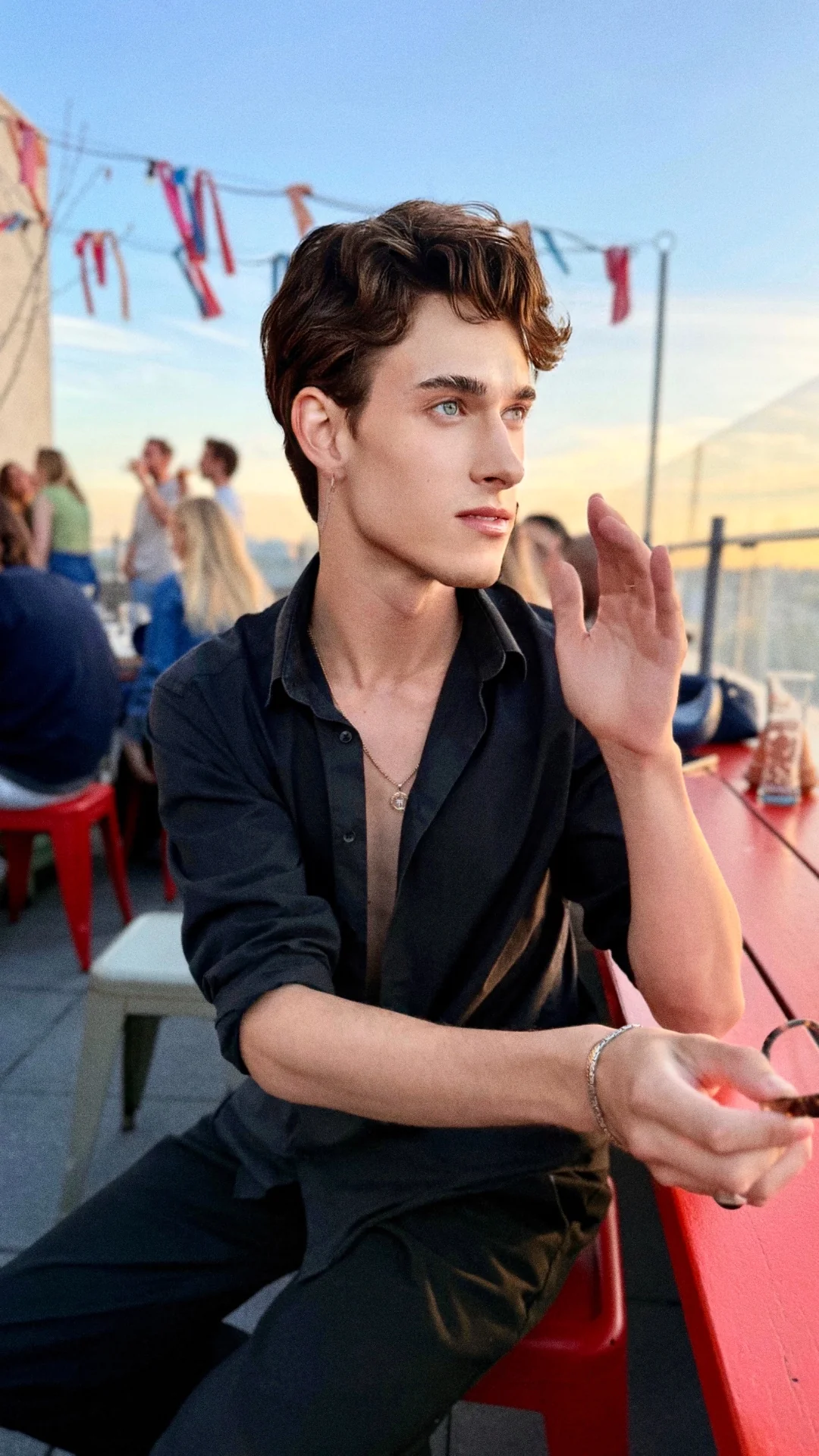 Jules Sauvage, escort gay Paris — soir d'été sur un rooftop parisien sous guirlandes lumineuses